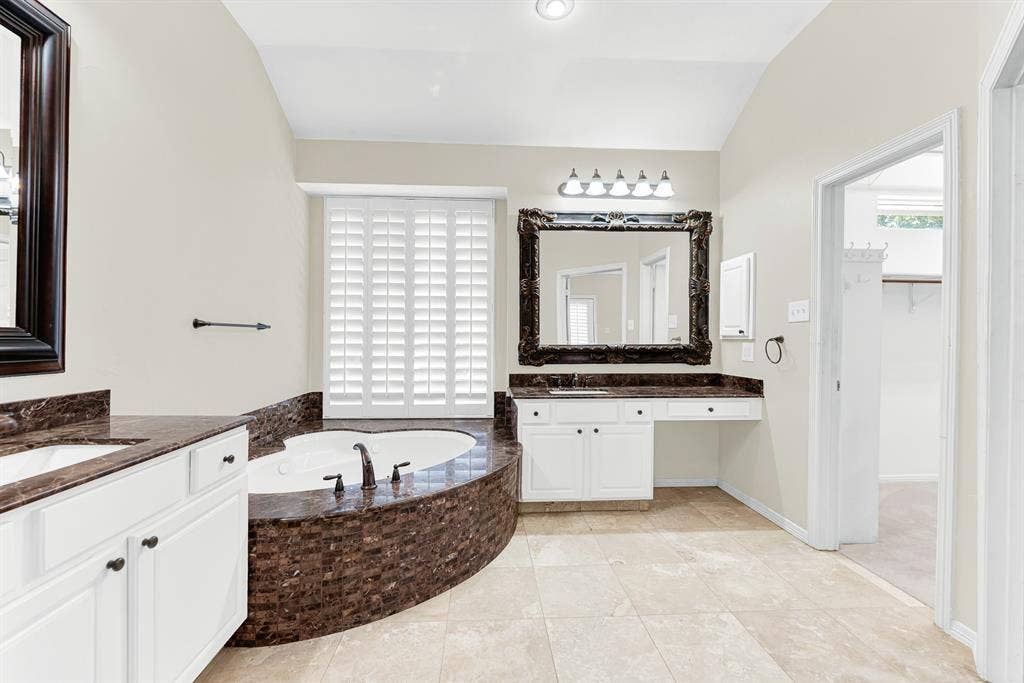 3217 Royal Melbourne Drive, Plano, TX 75093 Looking across the tiled floor reveals a dedicated vanity seating area with a large carved mirror, plantation-shuttered window, and a door into the walk-in closet. It creates a convenient, organized environment that makes getting ready for morning routines or evening events effortless.