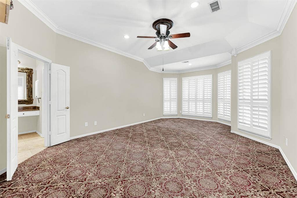 3217 Royal Melbourne Drive, Plano, TX 75093 An elegant tray ceiling with crown molding caps this primary suite, featuring pattern carpeting, a ceiling fan, and direct access to the en-suite bath. It creates a serene, restful haven where you can unwind in total comfort after a long day.