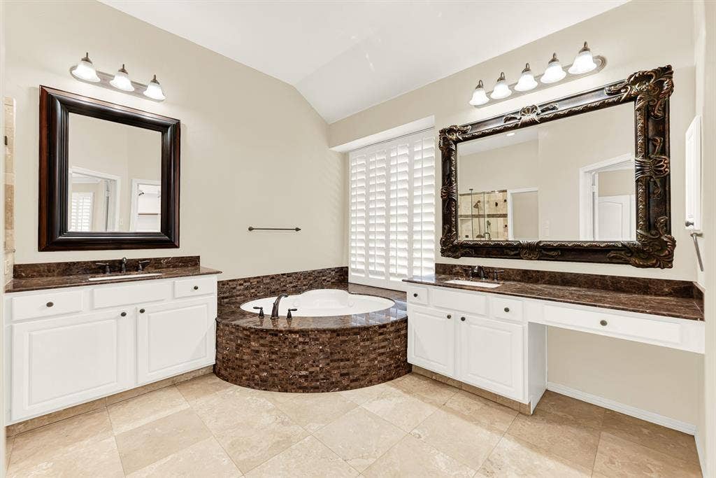3217 Royal Melbourne Drive, Plano, TX 75093 A luxurious corner soaking tub wrapped in rich mosaic stone serves as the centerpiece, flanked by dual white vanities with dark granite tops. It offers a spa-like retreat where you can soak away the day in total calm and luxury.