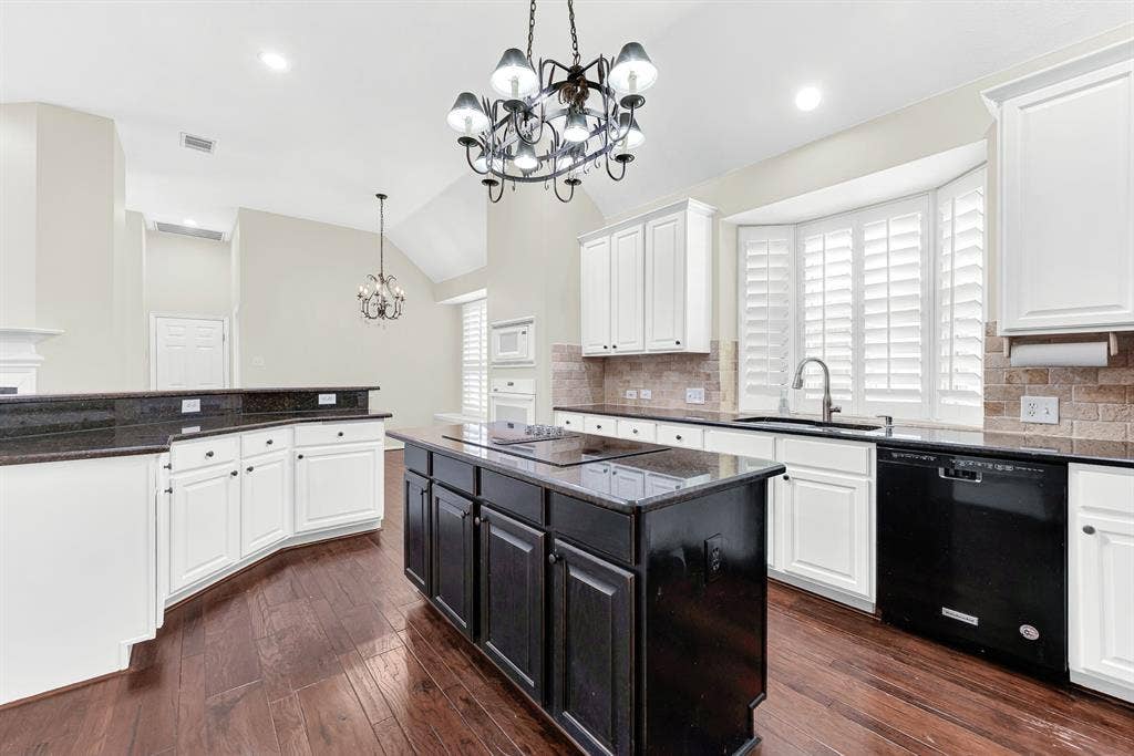 3217 Royal Melbourne Drive, Plano, TX 75093 Looking across the dark granite island, this angle showcases the bright bay window over the sink, gleaming dark hardwood floors, and extensive counter space. It offers a warm setting to enjoy morning prep while daylight streams in through the shutters.