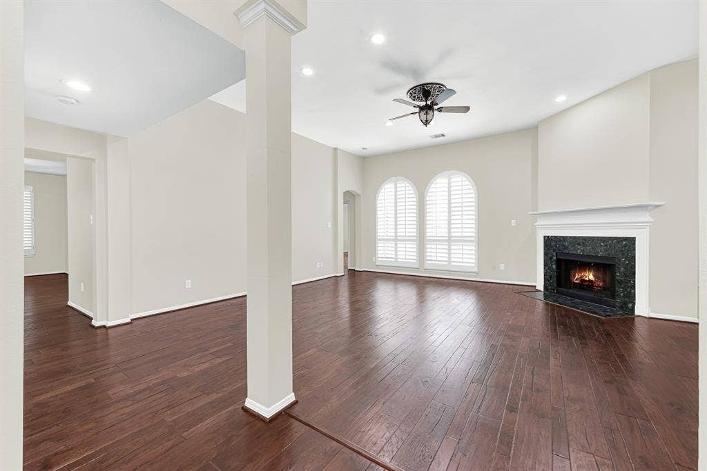 3217 Royal Melbourne Drive, Plano, TX 75093 Rich hardwood flooring leads toward a cozy black-tile surround fireplace, framed by arched windows with plantation shutters and clean architectural columns. It is the ultimate spot to curl up with a cup of coffee on cool evenings or relax after a busy workday