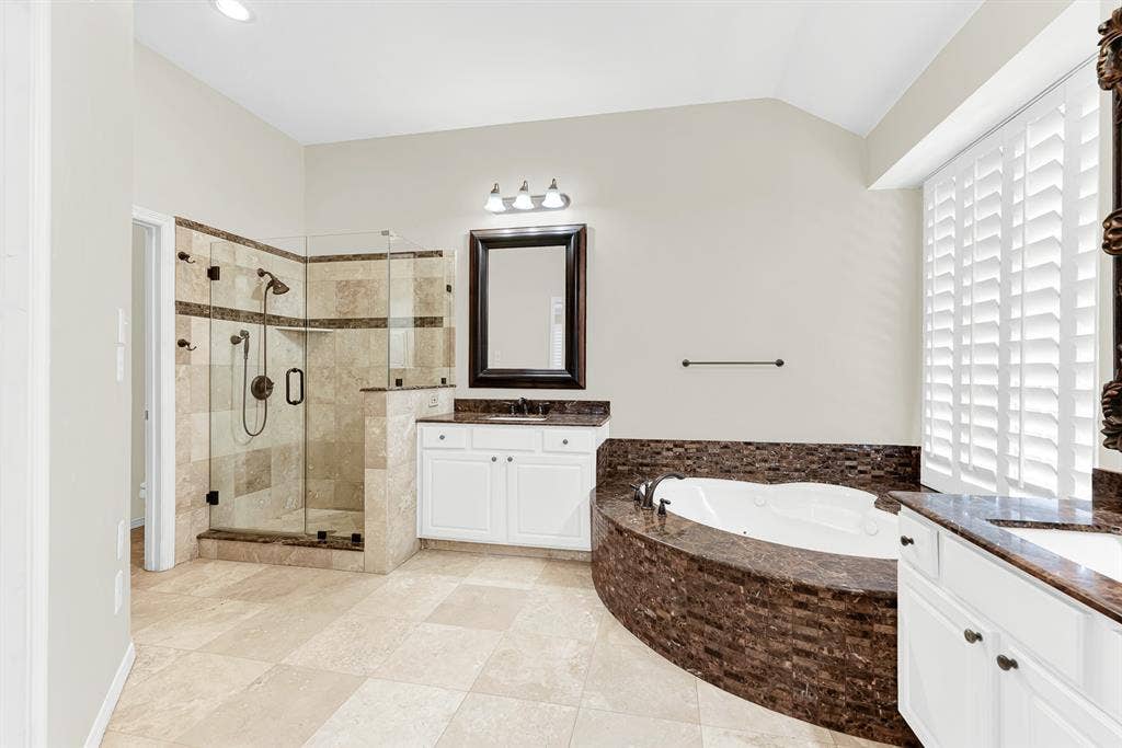 3217 Royal Melbourne Drive, Plano, TX 75093 This angle highlights a seamless glass-enclosed walk-in shower lined with travertine tile, positioned right beside the deep soaking tub and vanity area. You will love having a bright, invigorating space to quickly refresh every morning before taking on the day.