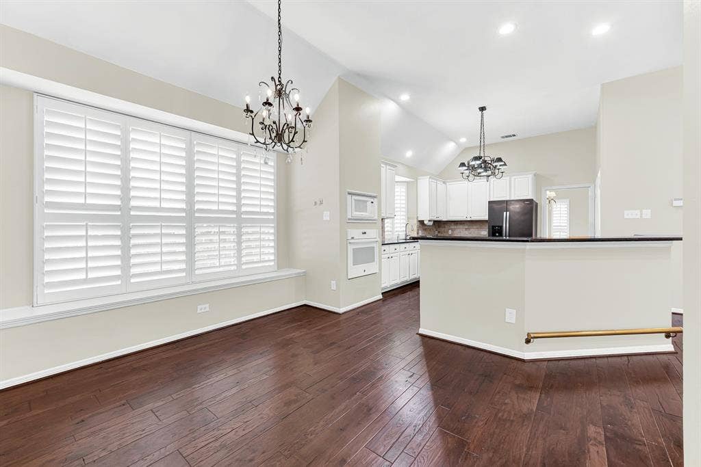 3217 Royal Melbourne Drive, Plano, TX 75093 Framed by vaulted ceilings and dual chandeliers, this shot shows the easy transition from the window-lit dining area to the kitchen bar. It provides a versatile space where family dinners can naturally extend into casual evening conversations.