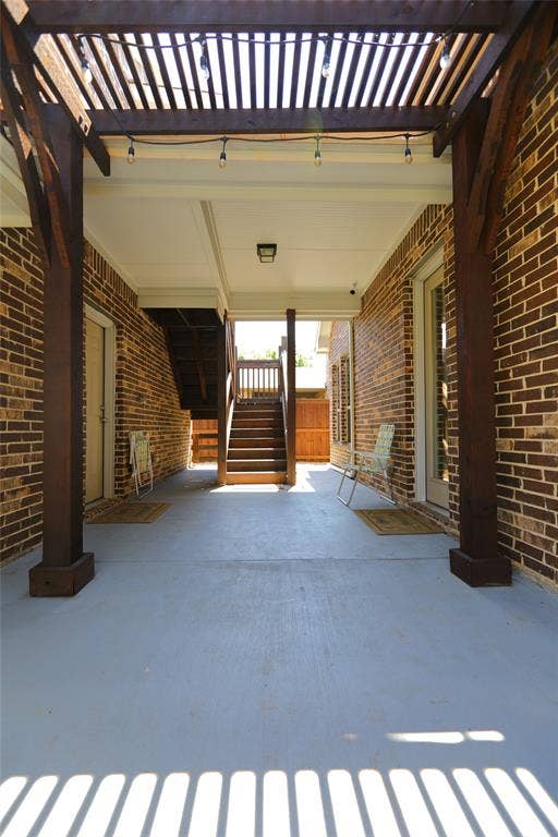 3707 Plum Vista Place, Arlington, TX 76005 Spacious patio area featuring a slatted wood pergola with string lighting, brick exterior walls, and a light gray finished concrete surface