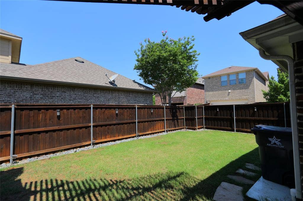 3707 Plum Vista Place, Arlington, TX 76005 Grassed backyard with a privacy fence featuring integrated lighting, stone paver accents, and a covered patio area