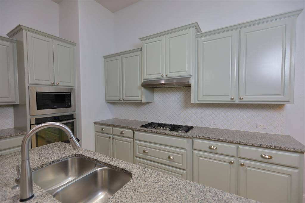 3707 Plum Vista Place, Arlington, TX 76005 Kitchen featuring light grey cabinetry, stainless steel appliances, a gas cooktop, white tile backsplash with a diamond pattern, and granite countertops