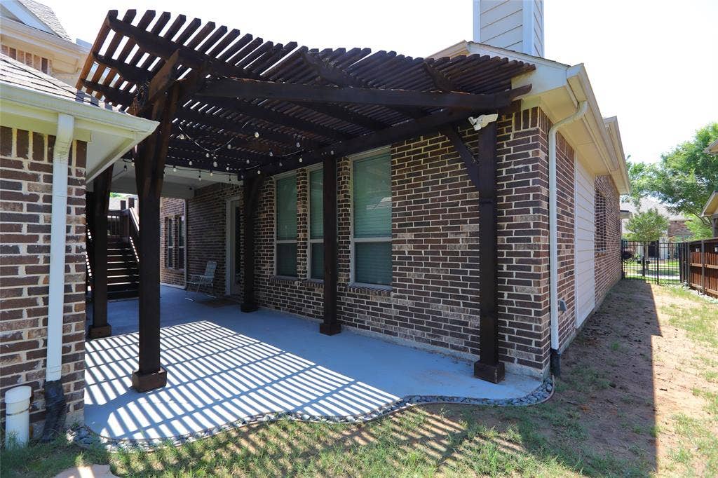 3707 Plum Vista Place, Arlington, TX 76005 Expansive covered patio featuring a dark wood pergola, string lighting, brick exterior, concrete flooring, and a partial black metal fence