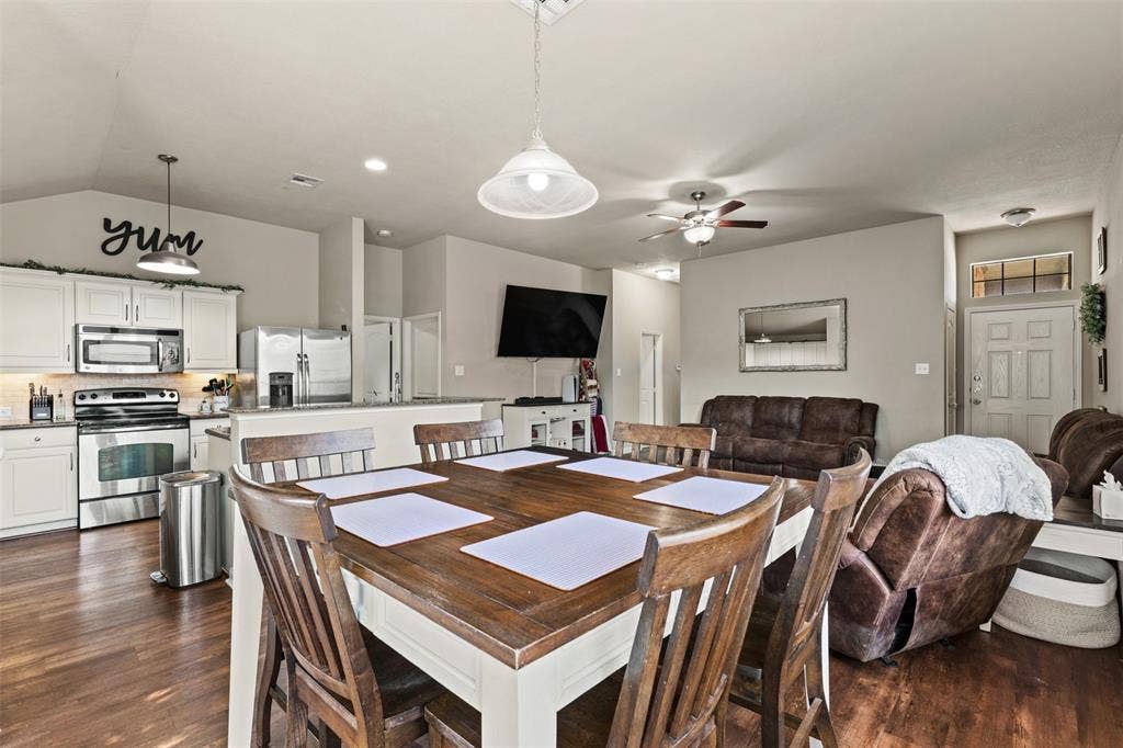 10313 Condor Loop, Waco, TX 76708 Open-concept living space with wood-finish flooring, a kitchen featuring white cabinetry and stainless steel appliances, and a dining area with a wood-top table