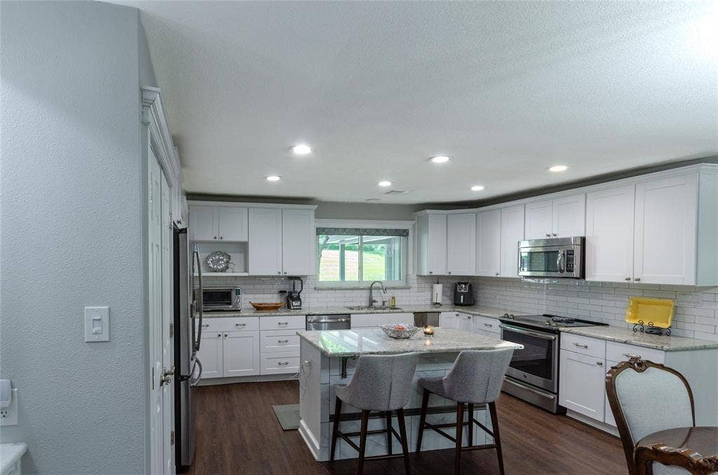 3613 Windmill Hill Street, Waco, TX 76710 White shaker cabinetry, stainless steel appliances, wood-finish flooring, recessed lighting, and a kitchen island with seating