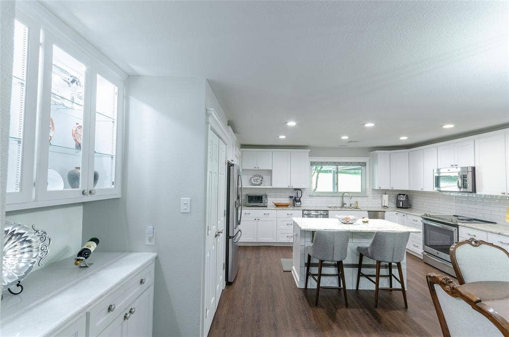3613 Windmill Hill Street, Waco, TX 76710 White cabinetry with glass-front uppers, stainless steel appliances, a center island with seating, and wood-finish flooring
