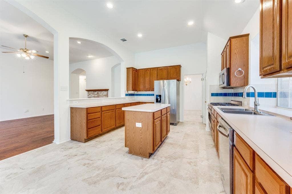 The kitchen features a central island, wood cabinetry, a recently replaced stainless steel stove, stovetop, & microwave, and a tile backsplash.  The picture is taken from the breakfast area directly connected to the kitchen.