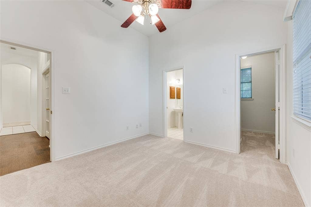 This 4th bedroom is in the front east corner and has its own bathroom.  It has a vaulted ceiling, a ceiling fan & light fixture, neutral wall color, plush carpet flooring, and a window with blinds. The study is on the right down the short hallway.