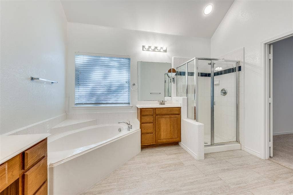 Spacious bathroom featuring a built-in soaking tub, separate glass-enclosed shower, a vanity with wood-finish cabinetry, and tiled flooring