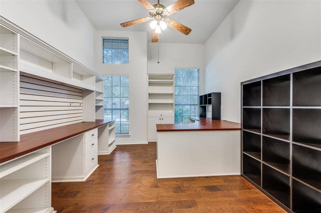 Dedicated workspace featuring extensive built-in shelving, two integrated desk surfaces, high ceilings, and wood-finish flooring.  A beautiful space for remote work.