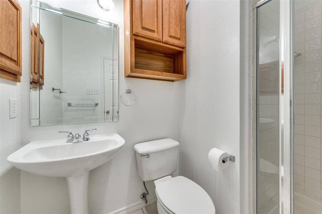 This 3rd bathroom is located within the 4th bedroom, so it will most likely be used exclusively by that occupant, and it's closest to the study.  It has a pedestal sink with a chrome faucet, a mirrored vanity, wood-finish wall cabinetry, and a shower enclosure with white tile