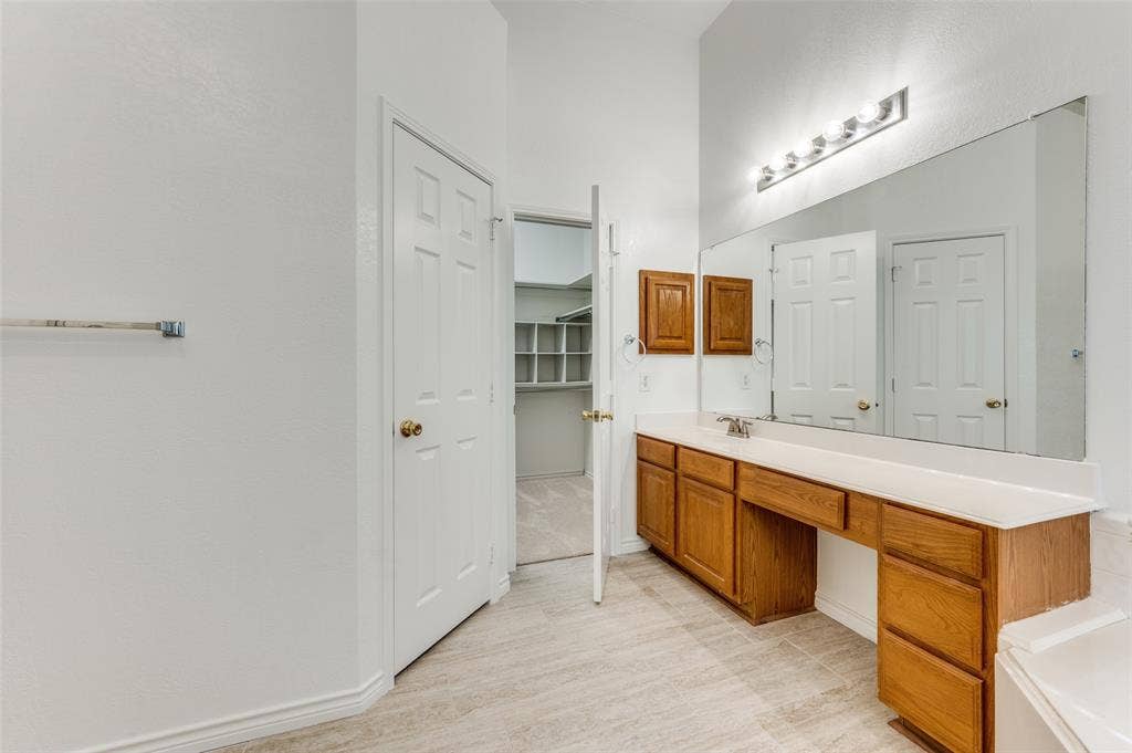White paneled door, wood-finish vanity with ample storage, integrated sink, and a large wall-mounted mirror with overhead lighting.  Nice large walk-in closet through the open door.  This picture doesn't show off the size of the closet.