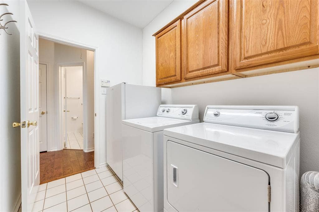 Laundry area with white tile flooring and overhead wood cabinetry.  This laundry room is located just off the 2nd and 3rd bedroom area for super convenience.