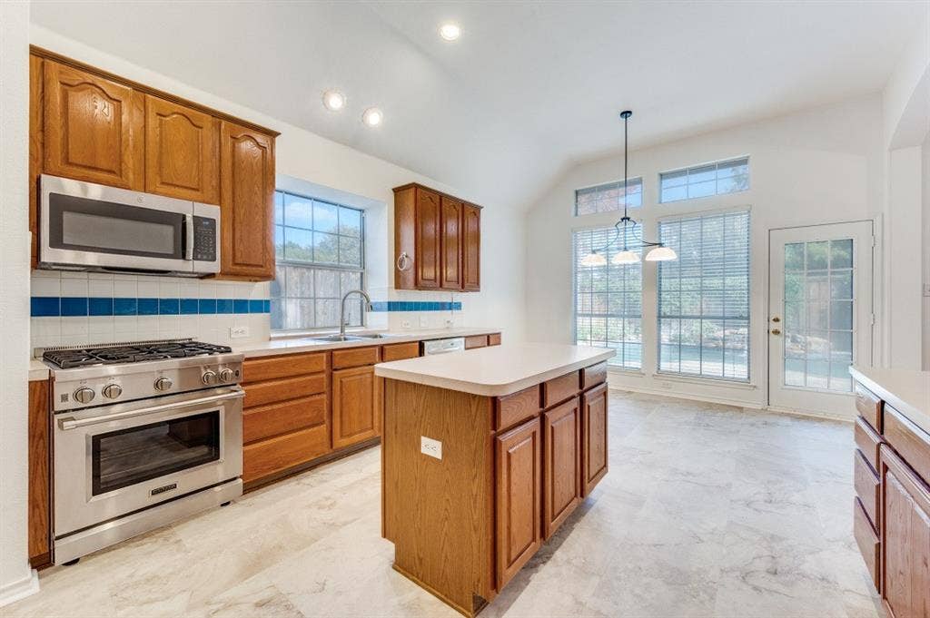 Kitchen featuring wood cabinetry, many recently replaced stainless steel stove, microwave, and cooktop, a center island, and a door leading to the beautiful private pool area in the back.