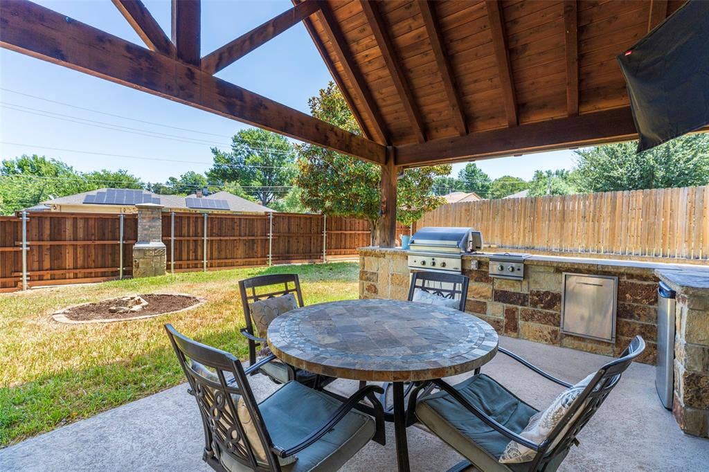 1620 Babbling Brook Drive, Grand Prairie, TX 75050 Covered patio with exposed wood beam ceiling, built-in stone outdoor kitchen with grill, and concrete flooring