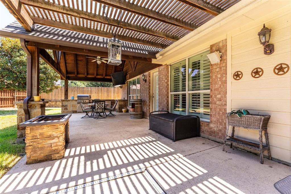1620 Babbling Brook Drive, Grand Prairie, TX 75050 Expansive covered patio featuring a wood pergola, stone-clad outdoor kitchen, ceiling fan, and concrete flooring