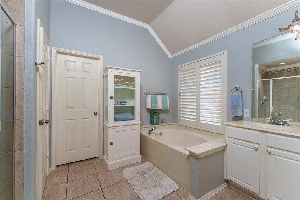 1620 Babbling Brook Drive, Grand Prairie, TX 75050 Vaulted ceiling, tiled flooring, built-in soaking tub, window with plantation shutters, and a single vanity with a mirror