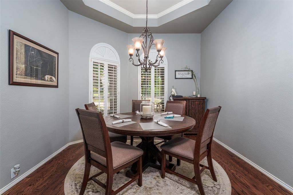 1620 Babbling Brook Drive, Grand Prairie, TX 75050 Tray ceiling, arched windows with plantation shutters, wood-finish flooring, and a decorative chandelier