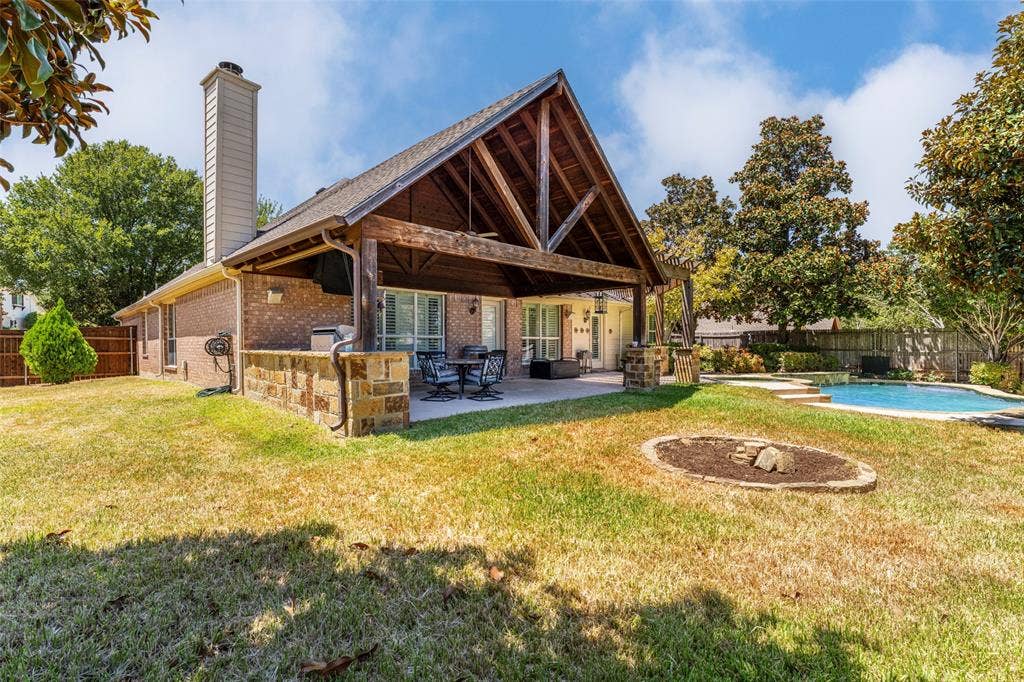 1620 Babbling Brook Drive, Grand Prairie, TX 75050 Expansive backyard featuring a covered patio with exposed wood beams, a built-in swimming pool, a brick exterior, and a dedicated fire pit area