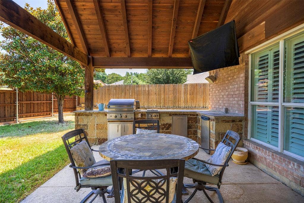 1620 Babbling Brook Drive, Grand Prairie, TX 75050 Covered patio featuring a built-in outdoor kitchen with grill, brick exterior, wood-plank ceiling, and privacy fencing