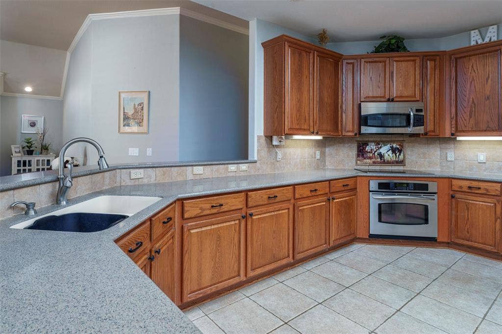 1620 Babbling Brook Drive, Grand Prairie, TX 75050 Kitchen featuring abundant wood cabinetry, integrated stainless steel appliances, speckled countertops, tile flooring, and a tile backsplash