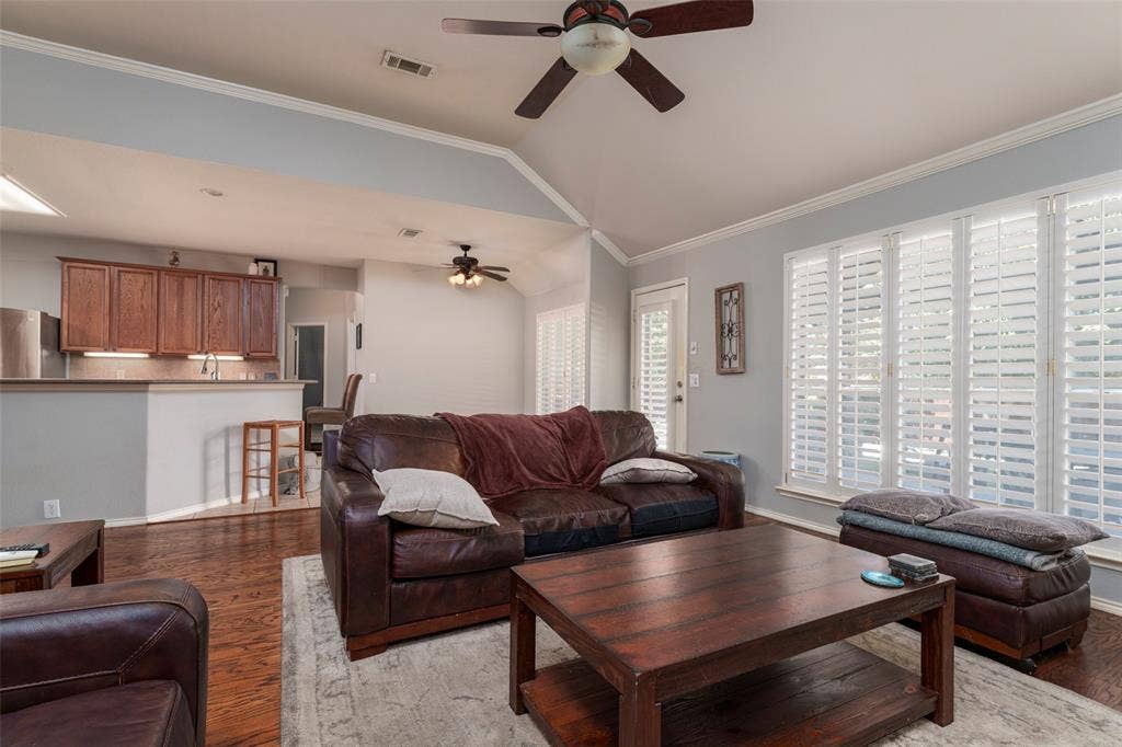 1620 Babbling Brook Drive, Grand Prairie, TX 75050 Vaulted ceiling with a ceiling fan, wood-finish flooring, kitchen pass-through with wood cabinetry, and large windows with plantation shutters