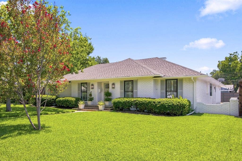 1409 Navaho Trail, Richardson, TX 75080 White painted brick exterior with dark shutters, prominent front entry, and a light-colored shingled roof