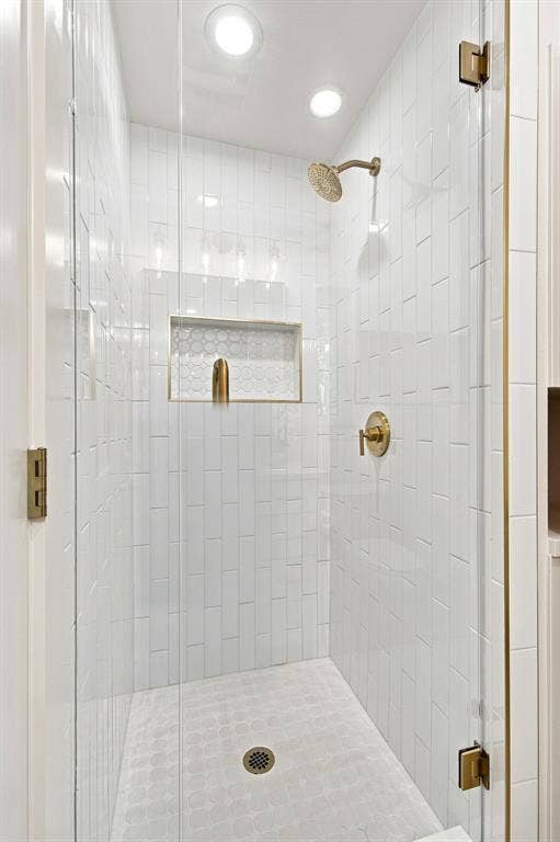1409 Navaho Trail, Richardson, TX 75080 Walk-in shower with clear glass enclosure and brass hardware, vertical subway tile surround, recessed niche with hexagon tile, and a circular tile shower floor