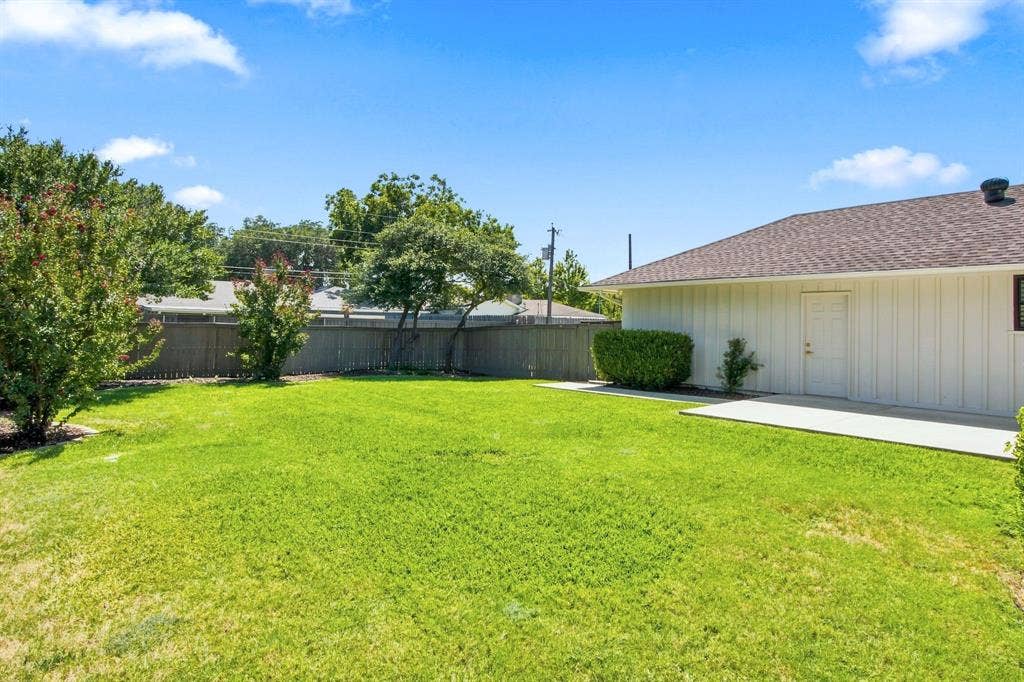 1409 Navaho Trail, Richardson, TX 75080 Expansive backyard with a lush lawn, privacy fencing, mature trees, and a concrete patio