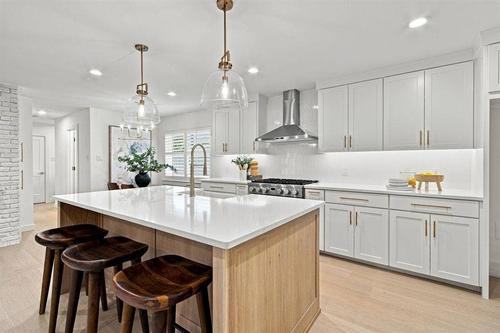 1409 Navaho Trail, Richardson, TX 75080 Kitchen featuring a center island with a stone countertop, white shaker cabinetry with gold-tone hardware, a stainless steel range hood, and wood-finish flooring