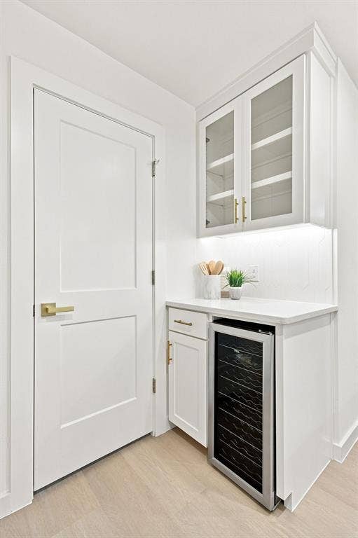 1409 Navaho Trail, Richardson, TX 75080 Built-in beverage refrigerator, white cabinetry with glass inserts, under-cabinet lighting, and light wood-finish flooring