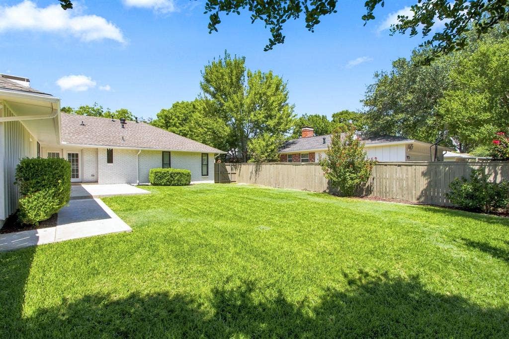 1409 Navaho Trail, Richardson, TX 75080 Expansive green lawn, concrete patio, mature perimeter trees, wood fence, and a white brick exterior