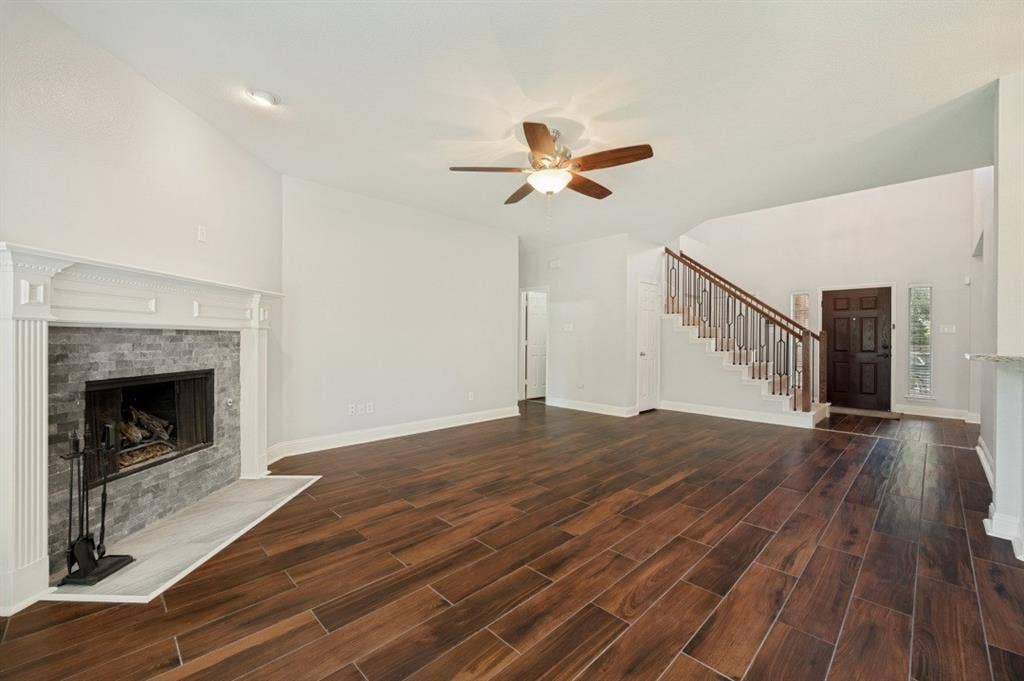 7900 White Stallion Trail, McKinney, TX 75070 Vaulted ceiling with a ceiling fan, wood-finish flooring, fireplace with stone surround and mantle, and a staircase with wood and metal railing