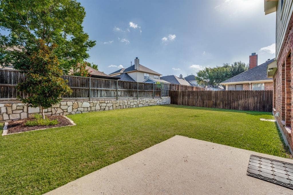 7900 White Stallion Trail, McKinney, TX 75070 Expansive green lawn, brick exterior, concrete patio, privacy fencing, and stone retaining wall