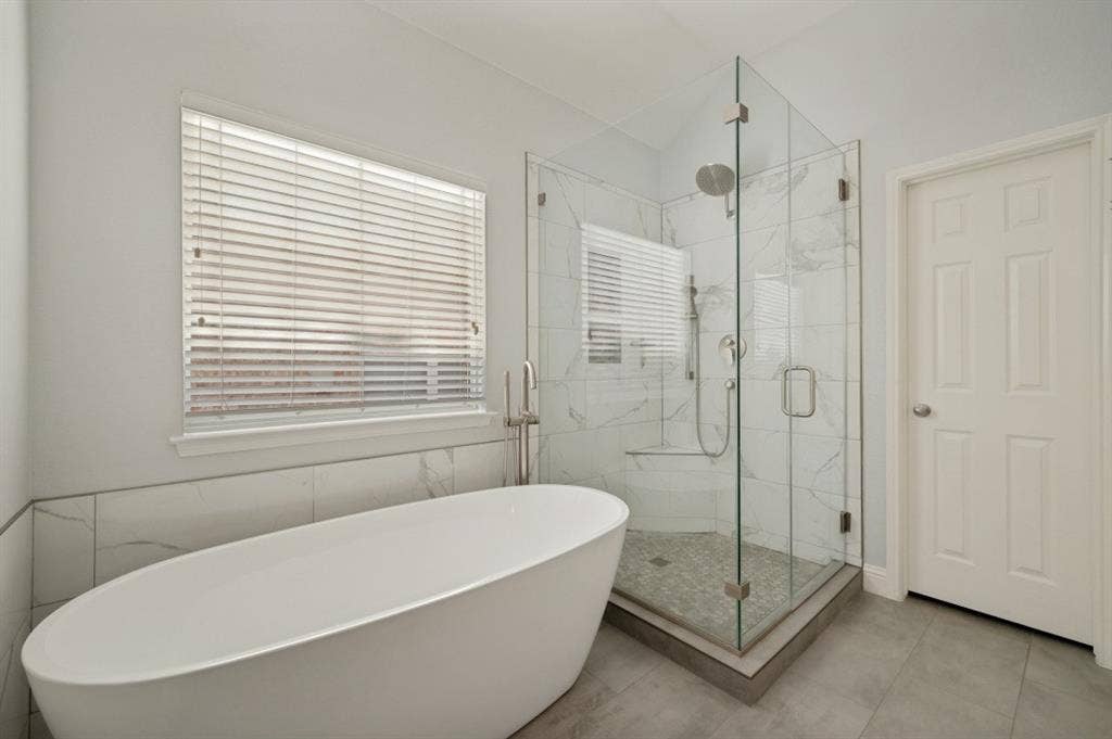 7900 White Stallion Trail, McKinney, TX 75070 Freestanding soaking tub with floor-mounted faucet, glass-enclosed shower with tile surround and bench, and large format tile flooring