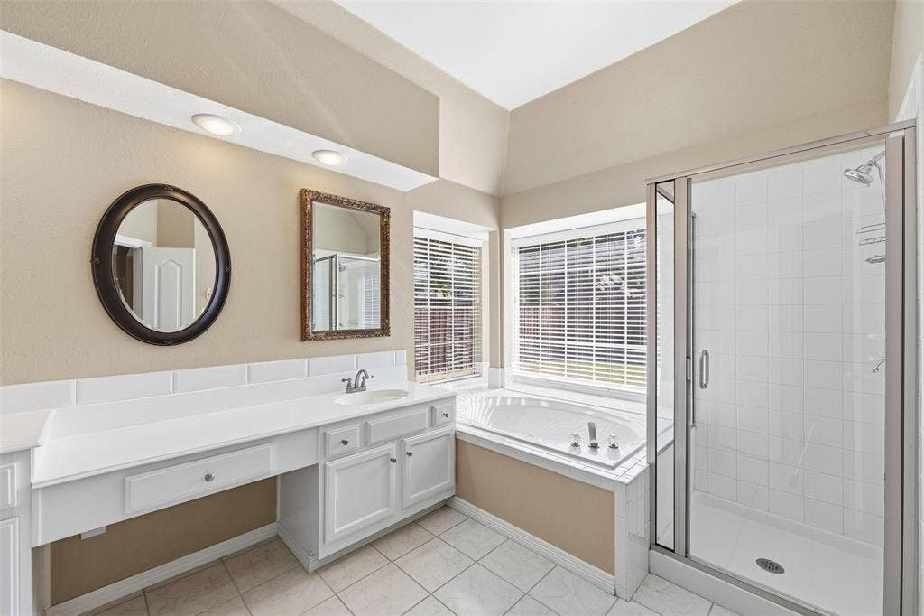 2910 Live Oak Drive, Rowlett, TX 75088 White vanity with integrated sink, expansive countertop, white tile flooring, built-in corner bathtub, and a glass-enclosed shower