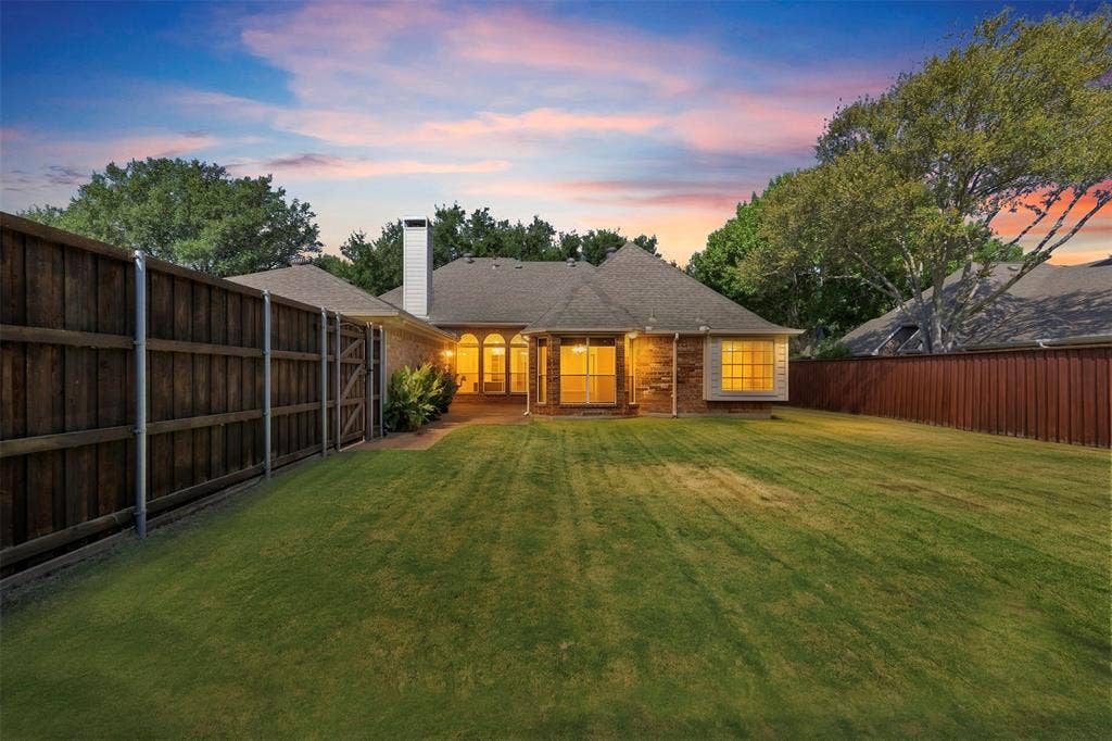 2910 Live Oak Drive, Rowlett, TX 75088 Expansive backyard featuring a manicured lawn, a full-height privacy fence, and a brick exterior with multiple windows