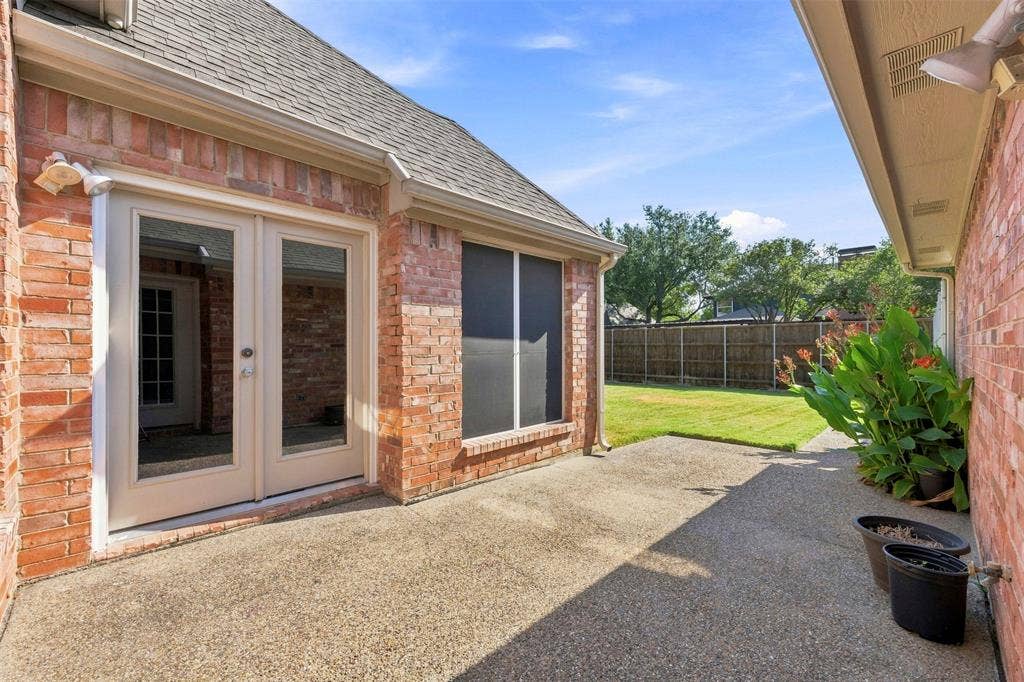 2910 Live Oak Drive, Rowlett, TX 75088 Brick exterior featuring a concrete patio, double glass-paneled doors, and a fenced backyard with a manicured lawn