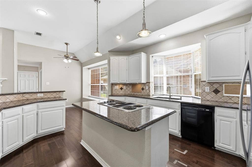 2910 Live Oak Drive, Rowlett, TX 75088 Kitchen featuring white cabinetry, dark wood-finish flooring, a central island with cooktop, black appliances, and a bay window
