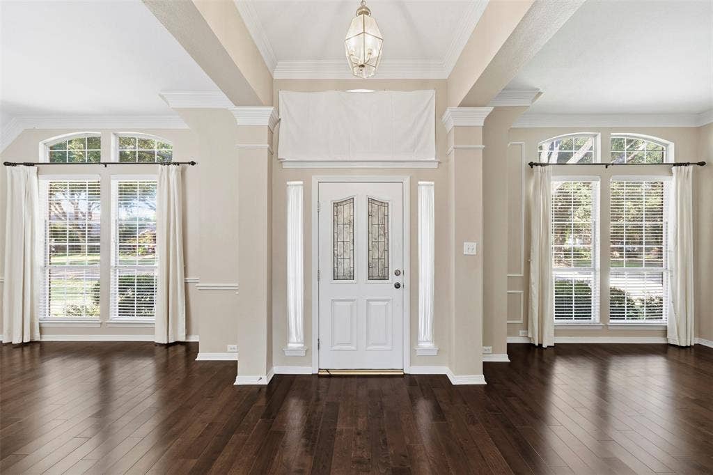2910 Live Oak Drive, Rowlett, TX 75088 Dark wood-finish flooring, white paneled entry door with decorative glass, arched transom windows, crown molding, and a decorative pendant light fixture