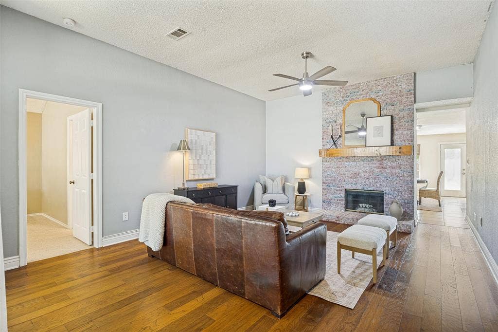 2922 Andrea Lane, Garland, TX 75040 Hardwood-finish flooring, a ceiling fan with integrated lighting, a brick fireplace, a wood mantel, and crisp white trim