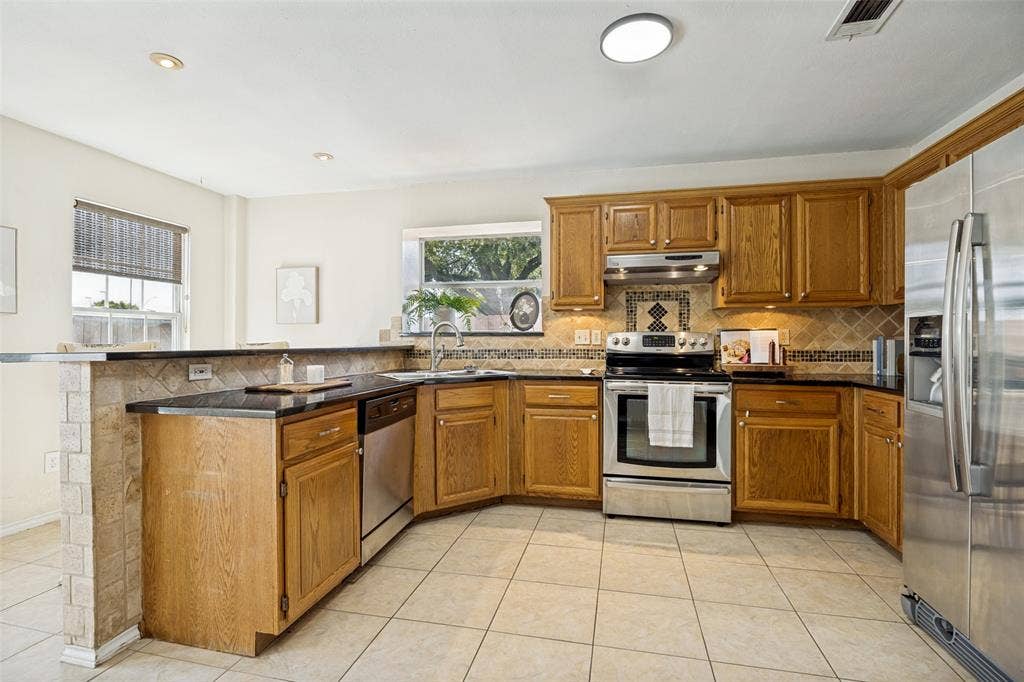 2922 Andrea Lane, Garland, TX 75040 Kitchen featuring wood cabinetry, black countertops, stainless steel appliances, and a tiled backsplash