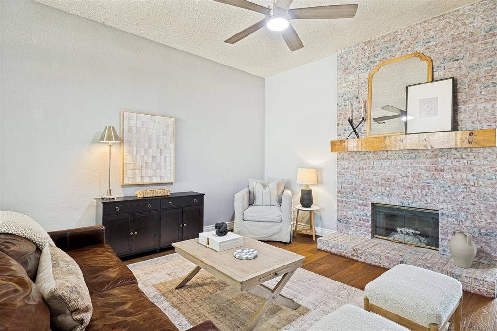 2922 Andrea Lane, Garland, TX 75040 Brick-clad fireplace with a wood mantel, wood-finish flooring, and a ceiling fan with integrated lighting