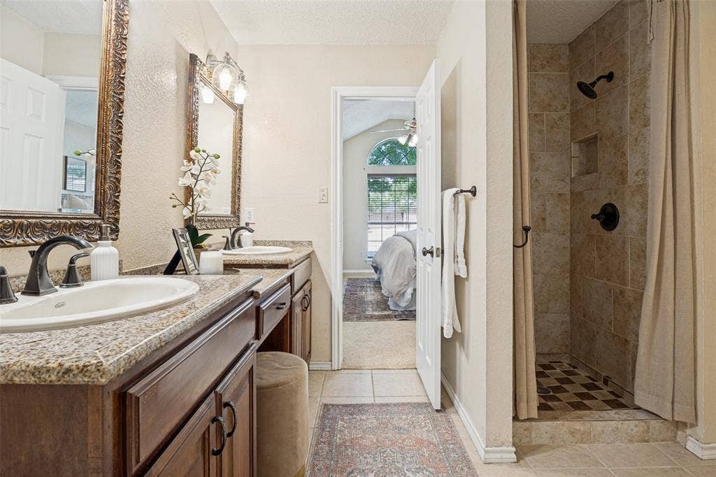 2922 Andrea Lane, Garland, TX 75040 Double vanity with granite-style countertops, dark wood-finish cabinetry, and oil-rubbed bronze fixtures