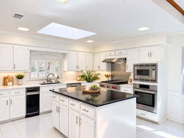 staged white cabinetry, stainless steel appliances, granite island countertop, white tile flooring, and a skylight