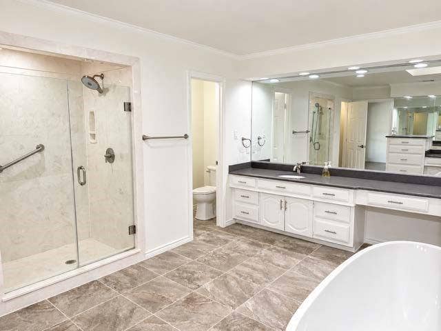 Glass-enclosed shower with stone-finish tile, extensive vanity with dual sinks, built-in makeup counter, and large wall-mounted mirror